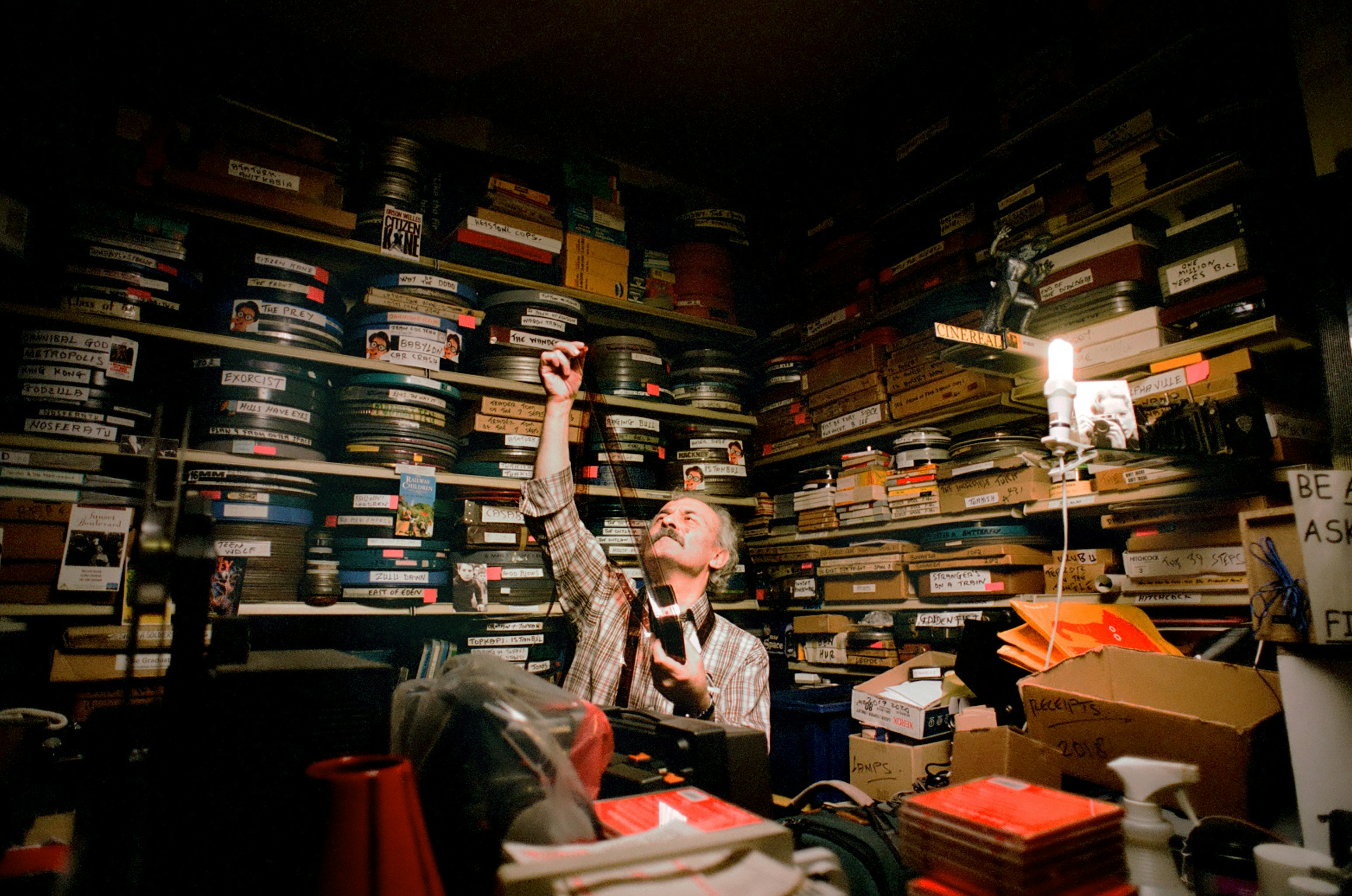 Ümit Mesut holding a strip of film among shelves filled with film cans