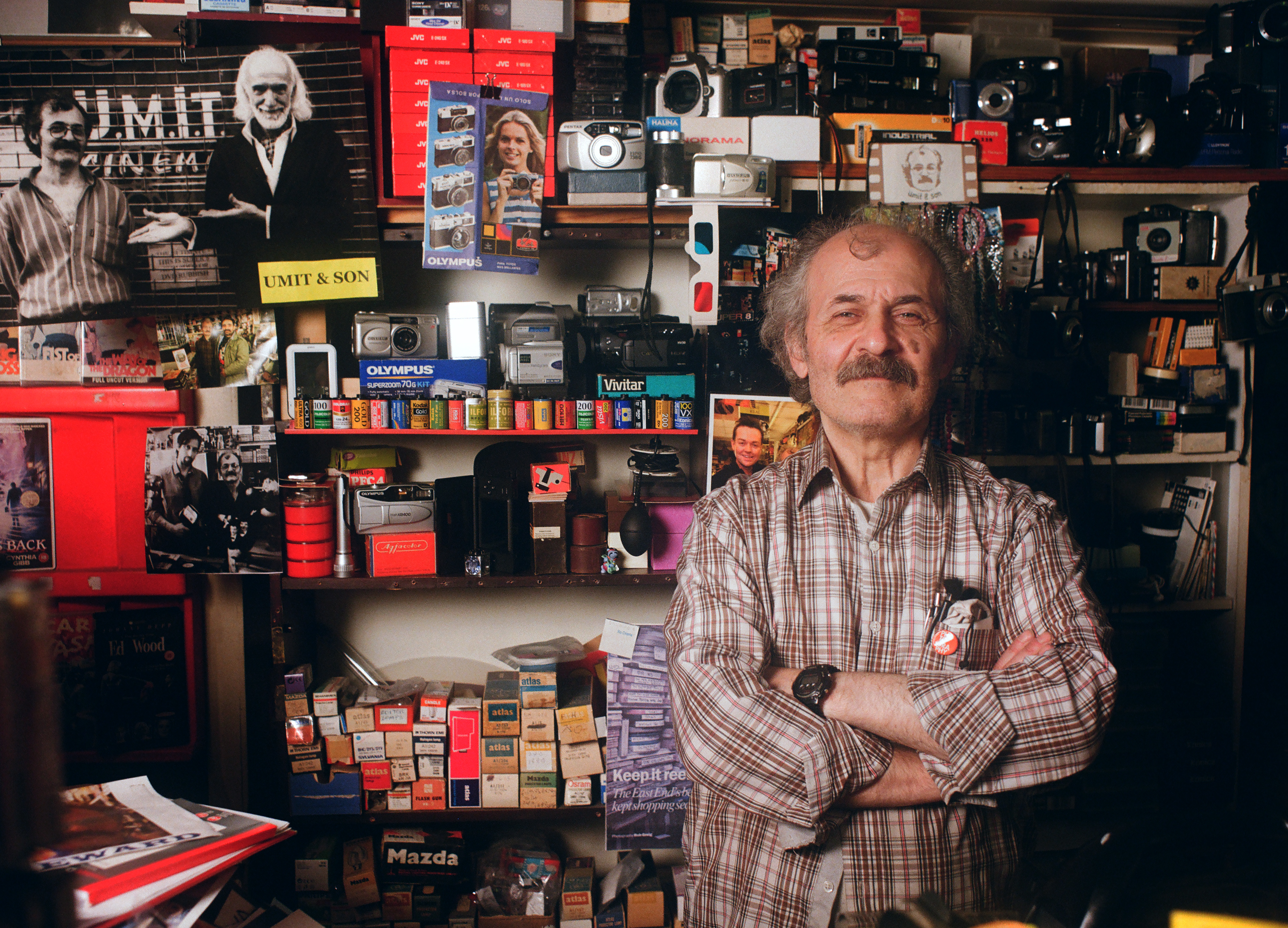 Ümit Mesut standing among cameras and film supplies in his shop